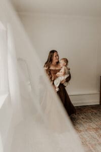 Mother holds her toddler daughter in a cozy, naturally lit photography studio in Mendham, NJ, styled with soft textures and warm, neutral tones—perfect for capturing connected, candid moments.